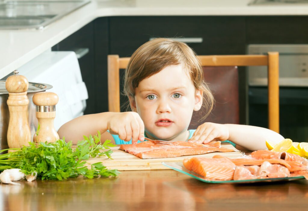 child with raw salmon fish in kitchen